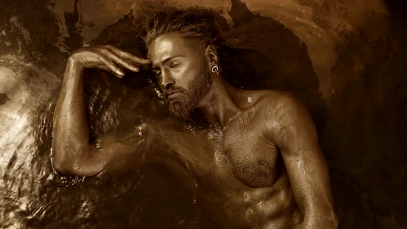 a Man Practices an Ecstatic Dance Lying in the Water in a Trance State with Golden Skin alt