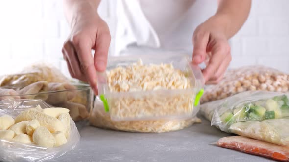 Woman puts container with frozen food, frozen grated cheese on table