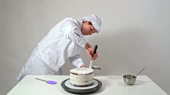Front Shot of a Baker Using an Icing Spatula to Carefully Touch Up Sides of Cream Covered Cake
