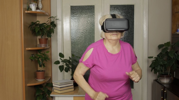 Senior Grandmother in Virtual Headset Glasses Watching 3D Video in VR Helmet and Running at Home alt