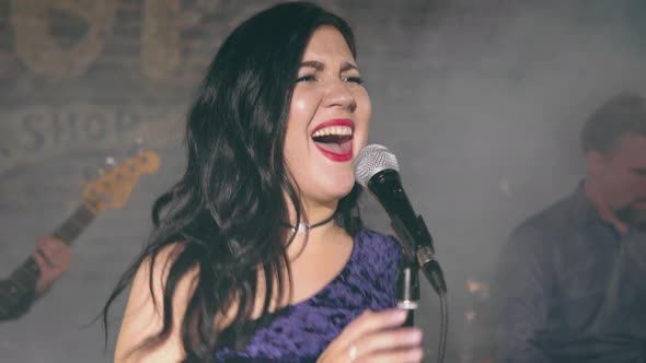 Pretty Female Vocalist Sings Into Microphone on Stage with Musical Group alt