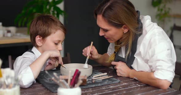 Mom and Her Son Draw a Clay Bowl Together in a Pottery Studio Workshop alt