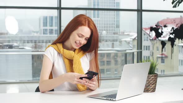 Beautiful Redhead Girl, Working in the Office, Uses a Laptop and Mobile Phone