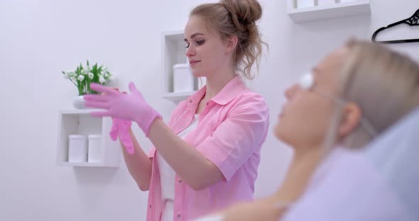 Female Beautician Puts on Gloves Before a Cosmetic Procedure alt