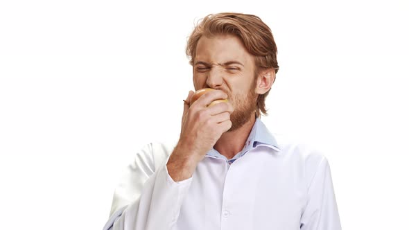 Strong Caucasian Young Doctor with Light Beard and Medical Overall Eating Apple Smiling on White alt