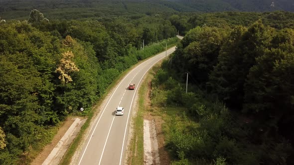 Orange SUV Car Driving on a Rural Road in the Mountains and Forest at Summer Sunny Day - Drone Point alt