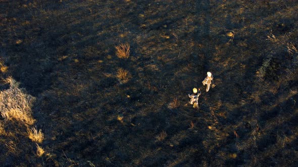 Two Firefighters Walk on Black Scorched Earth After Fire Dry Grass in a Field alt