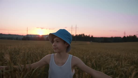 Funny Boy in a Hat a Golden Wheat Field at Sunset Against a Beautiful Sky Looking Around