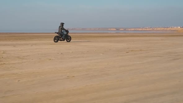 Motorcyclist Driving His Customized Fast Motorbike on the Dirt Road in Desert Around Sea or Lake alt
