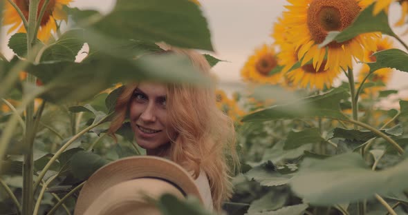 Beautiful Girl Takes Off Her Hat in a Sunflower Field Smiling