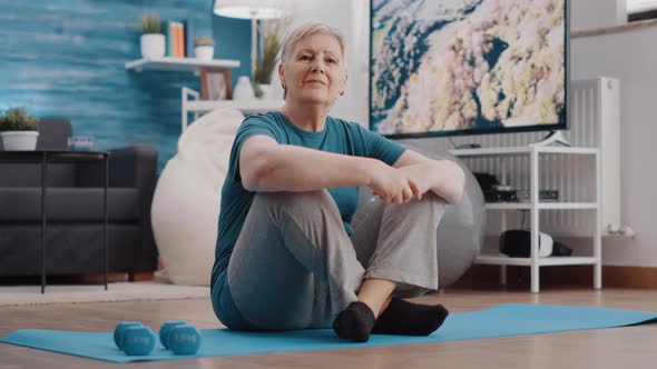 Portrait of Aged Woman Sitting on Floor Yoga Mat at Home alt