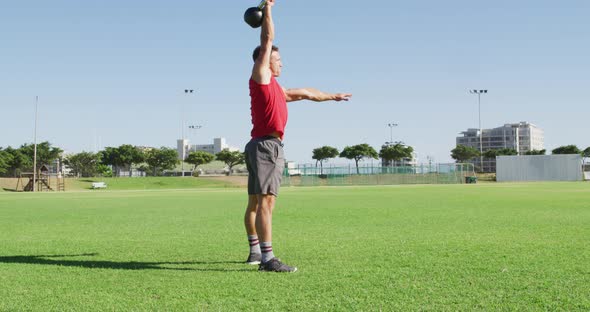 Fit caucasian man exercising outdoors, squatting and lifting kettlebell weight with one arm alt