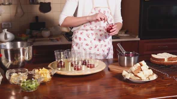 Chef Is Filling Glasses By Red Fruit Jam in a Home Kitchen, Standing Near Table alt