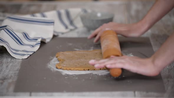Hands Roll Out the Dough with a Rolling Pin on a Table in the Kitchen Closeup