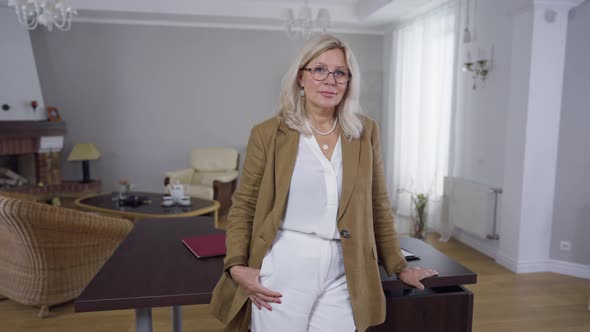 Blond Caucasian Woman in Eyeglasses Standing in Office at Table Looking at Camera Smiling alt