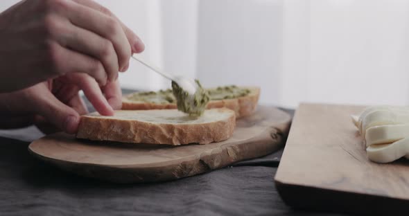 Slow Motion Man Making Ciabatta Bruschettas with Mozzarella and Pesto on Olive Board with Window on alt