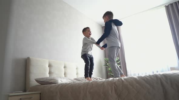 Two Little Brothers in Pajamas Cheerfully Jumping on Big Bed