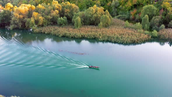 Small boat is sailing on the calm lake in autumn, leaving rippled trail behind