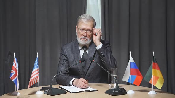 Portrait of Senior Bearded Businessman Sitting with Microphone in Boardroom During Meeting