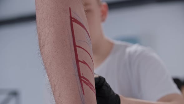 Young Man Drawing a Sketch for Tattoo on the Leg with a Red Marker alt