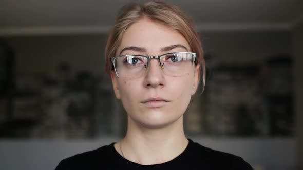 Portrait of attractive serious woman with glasses looking at camera indoor