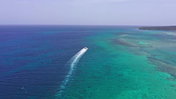 Boat sailing tropical waters near Playa Ensenada beach leaving white wake, Dominican Republic. Aeria alt