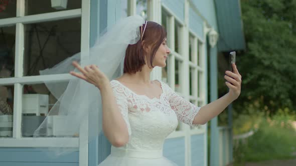 30s Bride in White Wedding Dress Taking Selfie Photos Standing Near Rural House alt
