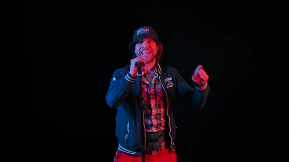 Charismatic Musician Sings Into a Microphone in a Dark Studio on a Black Background in the Light of alt
