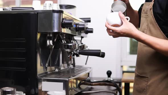 Male barista working in cafe pouring steamed milk into the cup making latte art coffee