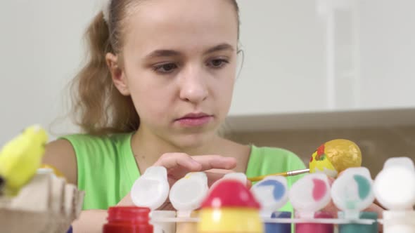 A Blonde Girl is Concentrating on Decorating an Easter Egg with Colors