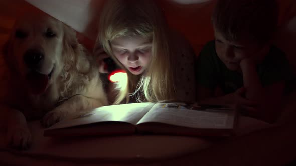 Happy Life with Pets - Little Children at Night Reading a Book Under the Covers with Their Big Dog
