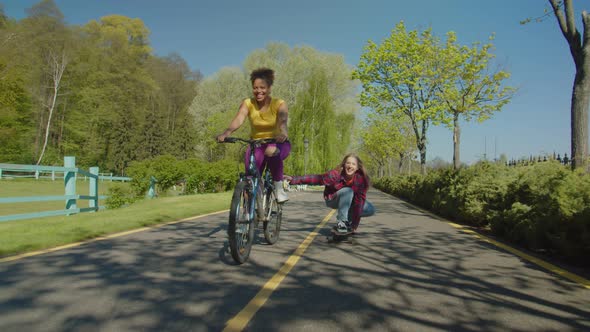 Cheerful Multiracial Females Enjoying Leisure Cycling and Skateboarding Outdoors alt