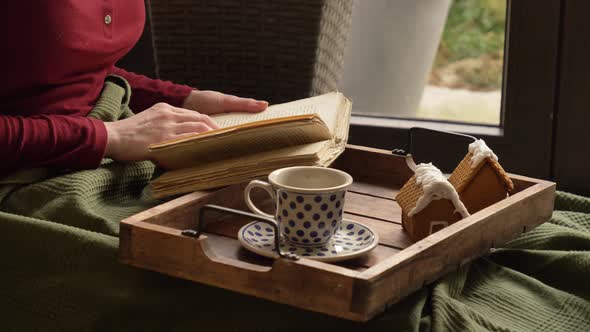 Woman drinking a coffee in a bed and reading a book.