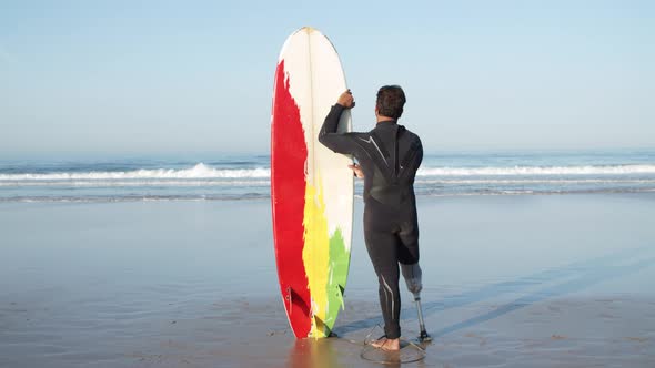 Back View of Surfer with Bionic Leg in Wetsuit Looking at Ocean alt