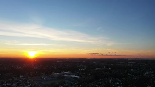 An aerial shot over a suburban neighborhood at sunrise. The camera slowly pan right along the horizo alt