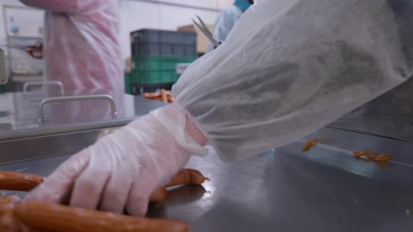 Workers of the Meat Processing Factory Separate Readymade Sausages with Scissors for the Packaging alt