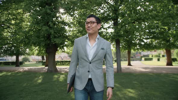 Korean Businessman Carrying Laptop Through Park alt