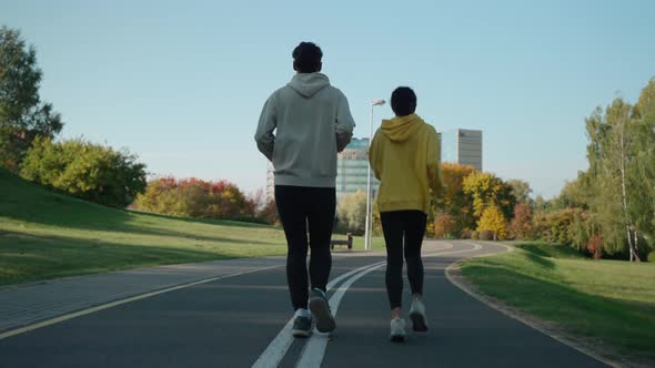 Man and Woman Running on a Track at the City Park in Sunny Autumn Morning alt