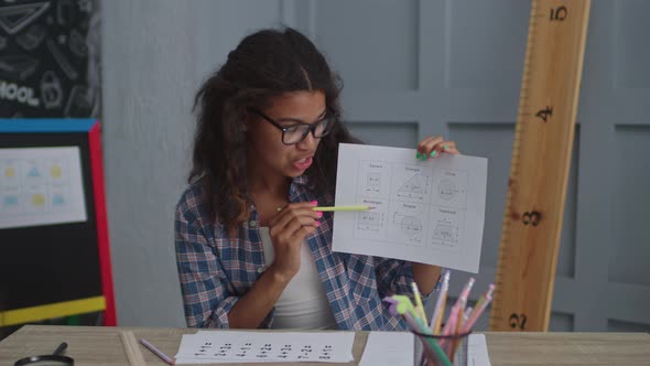 Female African American Geometry Teacher Speaking at Camera with Pupils and Showing Sheet of Paper alt