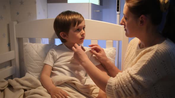 Mother Talking and Measuring Body Temperature of Her Little Son Feeling Unwell alt
