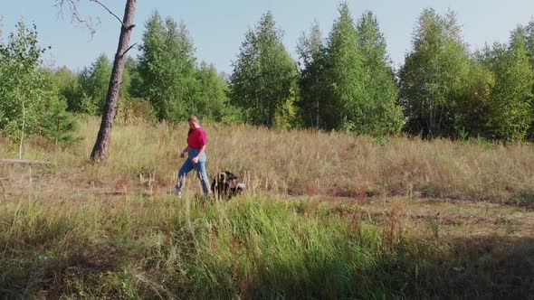 Young Woman and Her Cute Well Trained Dog Walking Together in the Edge of the Forest  Aerial View alt
