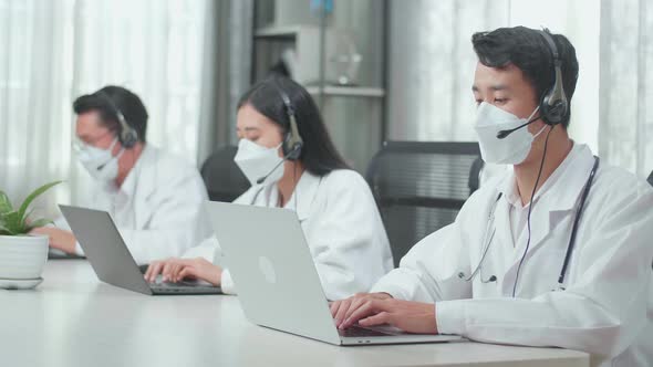 Three Asian Doctors With Stethoscopes Wearing Headsets And Masks Working As Call Centre Agents alt