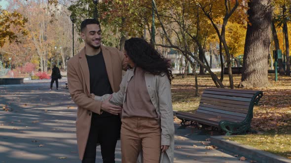 Joyful Hispanic Couple Cuddle Walking in Autumn Park Girl and Guy Holding Hands Lovers Embrace Laugh alt