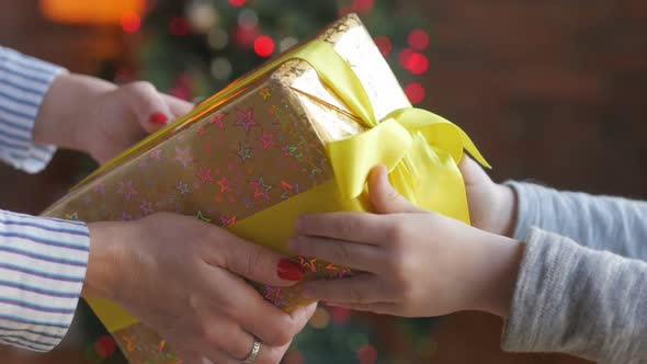 Mother gives a gift to her child against the backdrop of bright festive lights