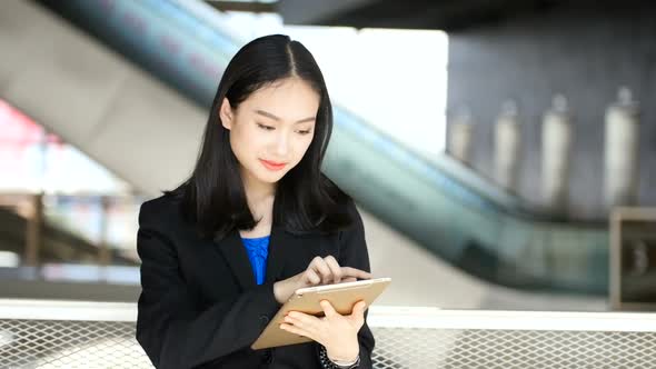 Asian girl holding a tablet playing social media on a building