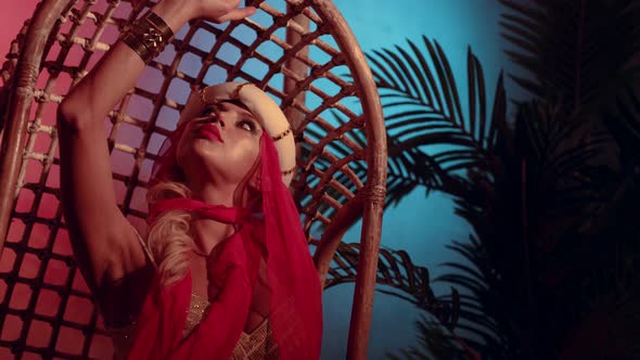 Portrait of a Woman in a Turban with a Red Scarf and a Sequined Dress in a Wicker Chair alt