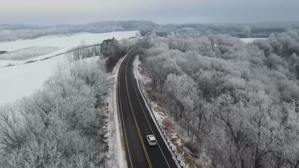 A drone view of a road in a forest covered in trees and snow shot in 4K