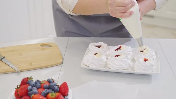 a Female Chef Adds Cream From a Pastry Bag to Anna Pavlova Cakes in the Kitchen alt