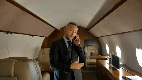 Businessman Talking on Cell Phone Indoor of Private Jet Cabin alt