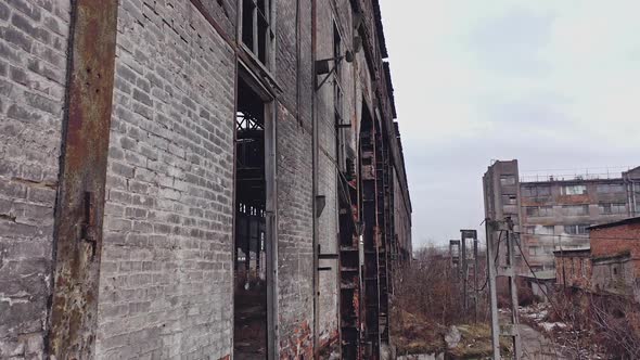Former plant building with damaged brick walls and metal structures covered with moss alt